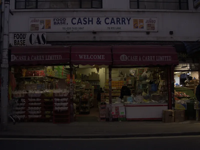 A Peckham cash and carry at dusk, its awning and window signs still lit