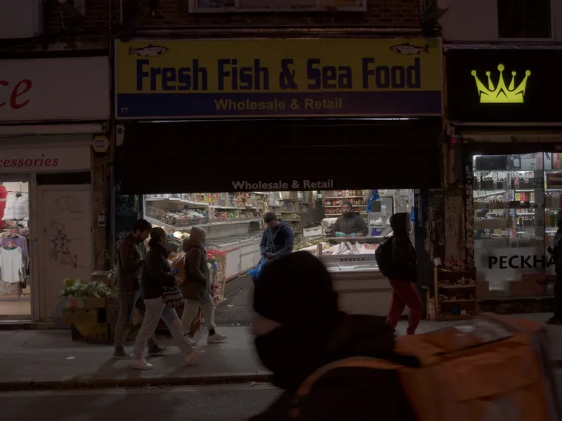 A fresh fish and sea food shop at night, people crossing in front of the window