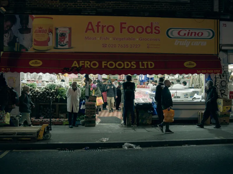 The yellow Afro Foods storefront after dark, shoppers gathered under the awning