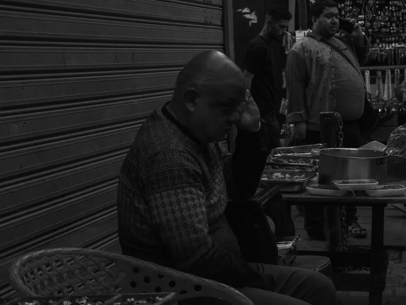 A man sitting alone at a cafe table in black and white, leaning over his drink