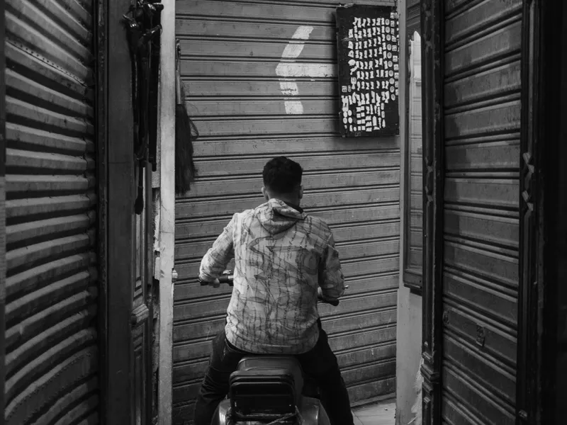 A man pushing a cart down a narrow alley of metal shutters, Arabic signage above