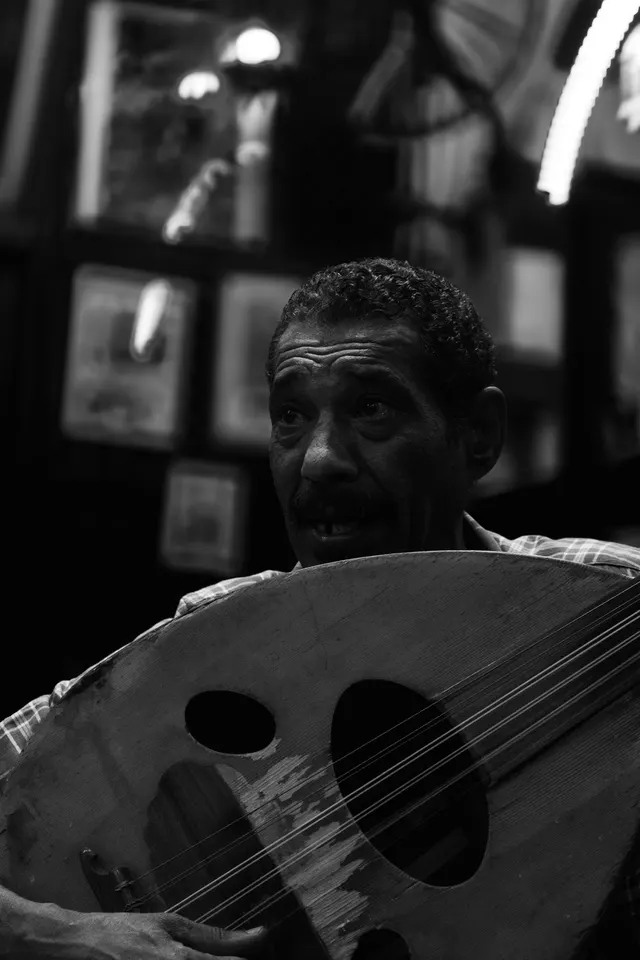 Black and white portrait of a man playing an oud in a dim room