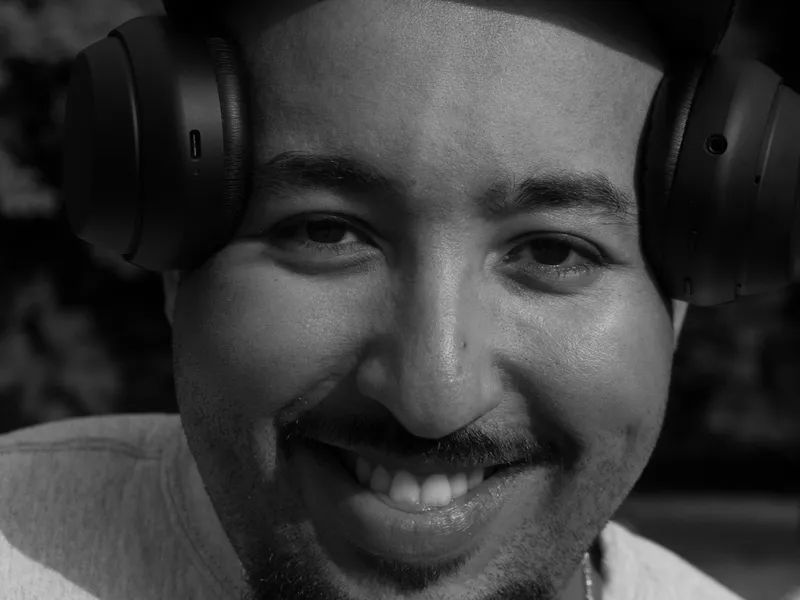 A man smiling wide with headphones around his neck, black and white