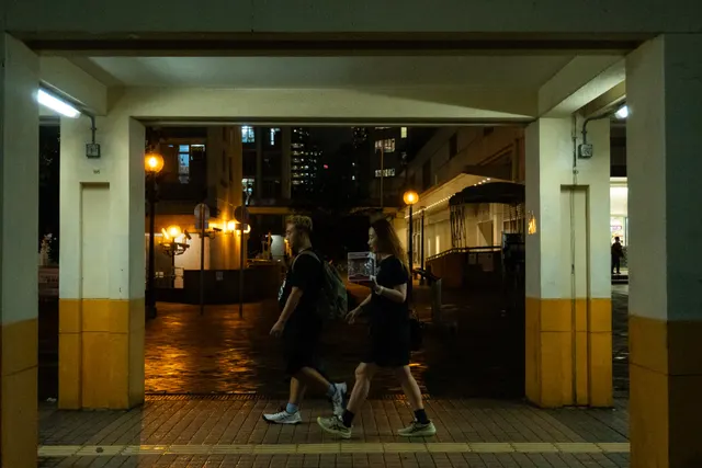 Figures running through a lit corridor at night, seen from the dark
