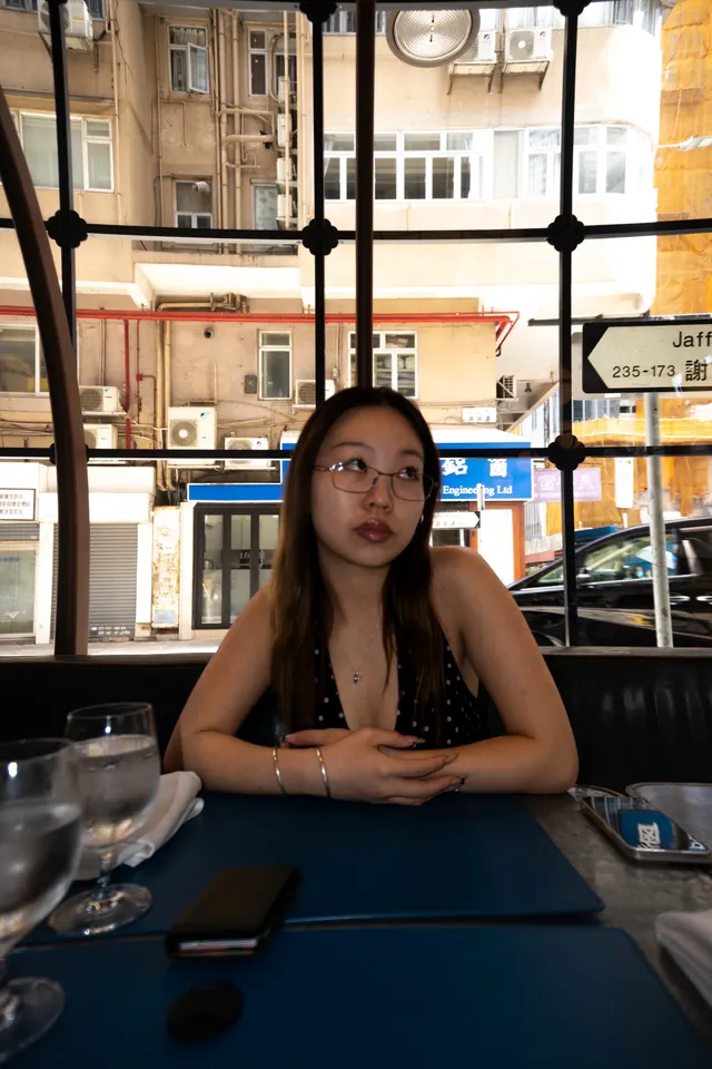 A woman at a restaurant window table, Hong Kong tower blocks behind the glass