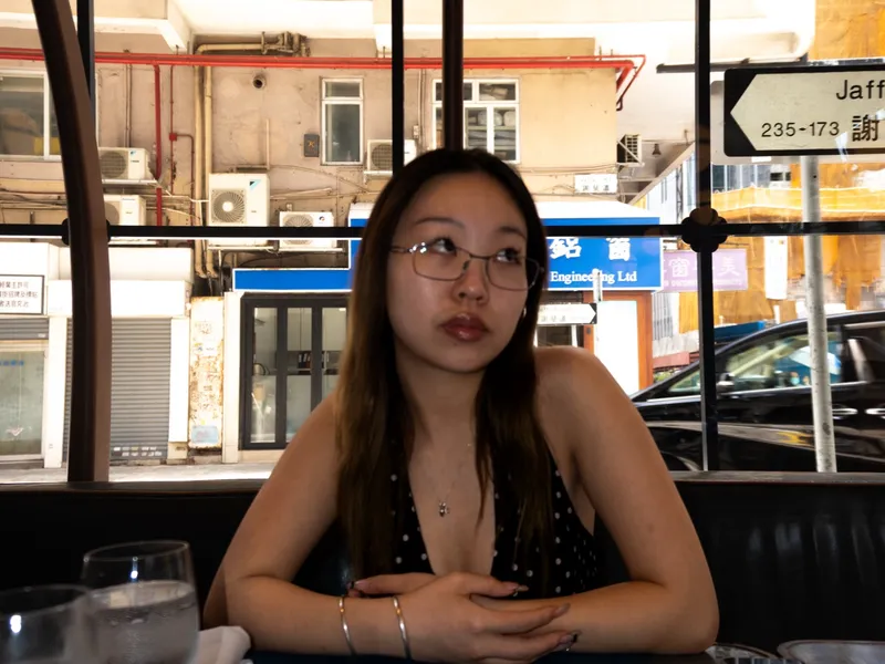 A woman at a restaurant window table, Hong Kong tower blocks behind the glass