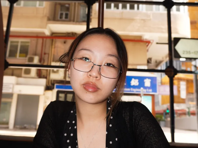 A woman in a polka dot top seated at a window, apartment blocks outside