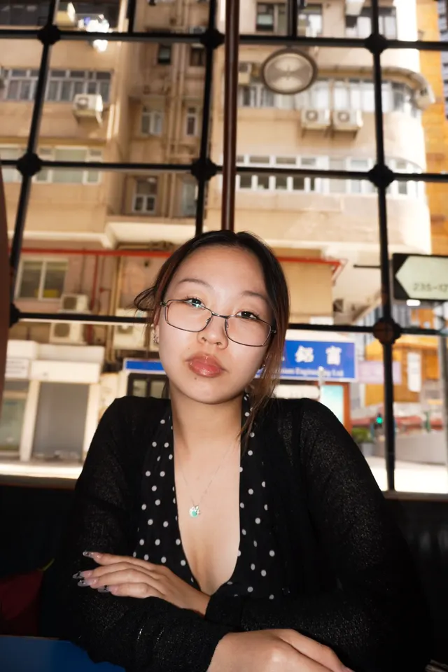 A woman in a polka dot top seated at a window, apartment blocks outside
