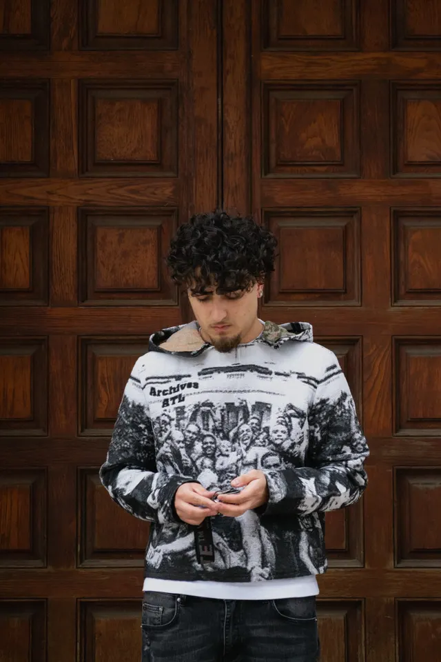 A young man in a patterned hoodie standing against a tall carved wooden door