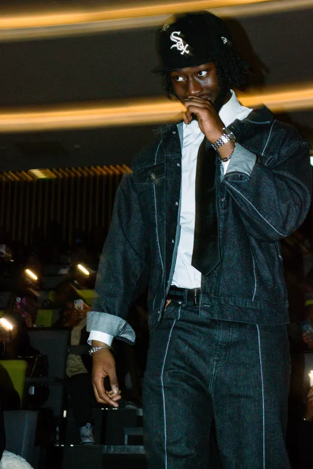 A man in a double denim suit and White Sox cap pausing at the end of a runway