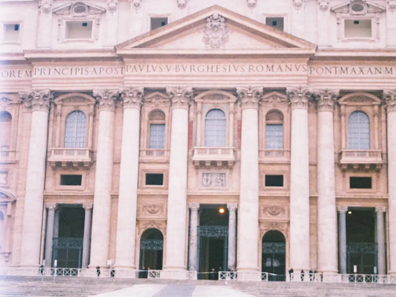 The facade of St Peter's Basilica in flat afternoon light, its inscription running the width of the frame
